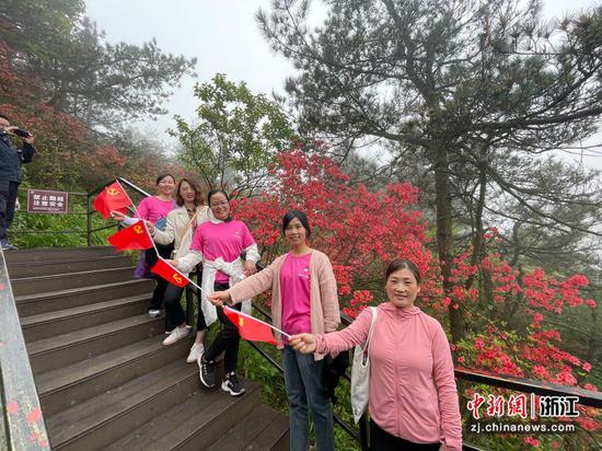 游客们手持党旗在杜鹃花前合影。  张斌 摄