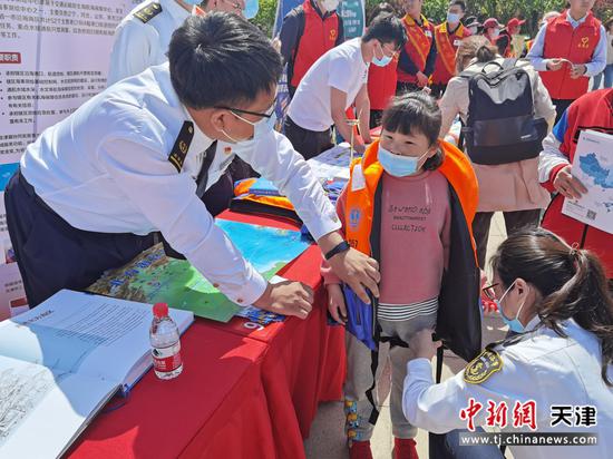 （集中服务活动现场，天津海事测绘中心工作人员协助小朋友穿戴救生衣并讲解。 王君妍 摄）