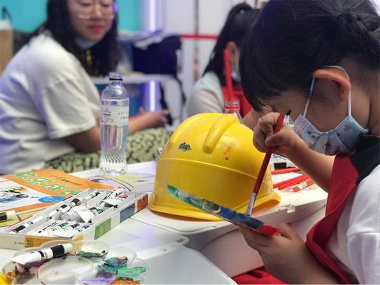 在乌鲁木齐经开区万达广场一楼国网新疆电力有限公司的智能电力体验馆内，7岁的柴羽诺正在安全帽上绘画。