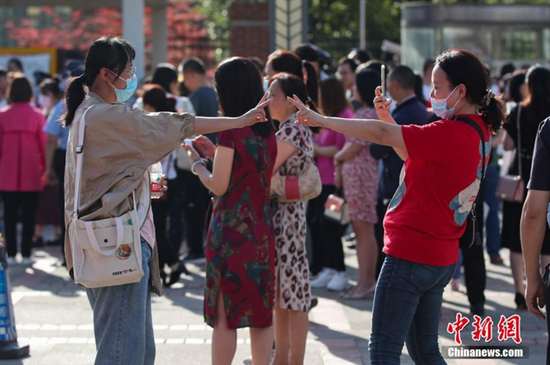 6月7日，贵州省遵义市汇川区遵义航天高级中学考点，一名考生（左）和家长在比“胜利手势”拍照。 中新社记者 瞿宏伦