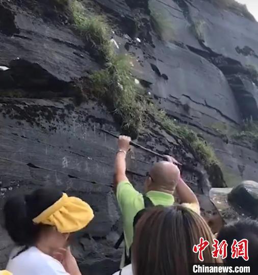 图为游客在梵净山一岩壁进行涂刻。　视频截图