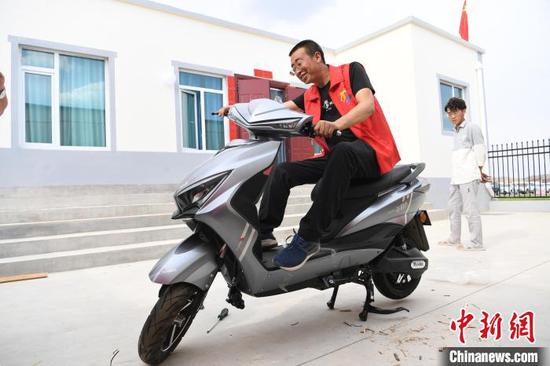 图为舟曲县搬迁移民刘石海在新家展示自己新买的电动车。　杨艳敏 摄