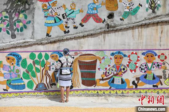 一名苗族画师在平坡村修补苗族绘画主题文化墙。　瞿宏伦 摄
