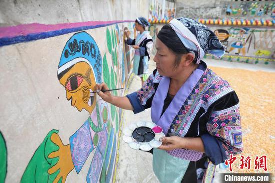 苗族画师在平坡村修补苗族绘画主题文化墙。　瞿宏伦 摄