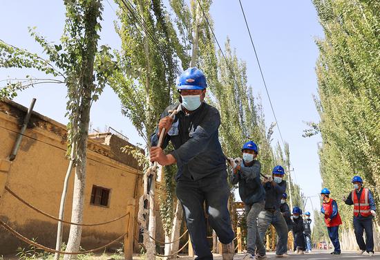 电力施工人员在新疆喀什地区英吉沙县一处“煤改电”施工现场准备架线。