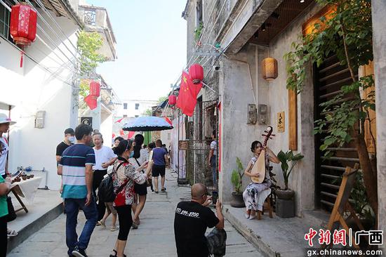 一名艺人在钦州市老街占鳌巷一家门店前弹琵琶，吸引游客驻足观看。曾开宏 摄