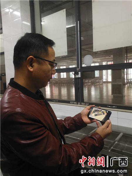 田东县第四中学副校长廖剑光正在用手机观看明厨亮灶摄像头监控画面。陈洁君 摄
