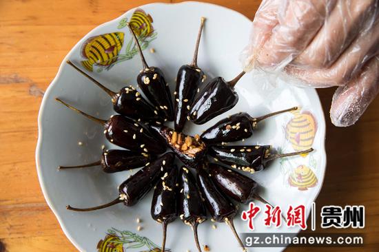 2021年12月7日，贵州省黔西市洪水镇官庄村一家特色辣味制作坊，村民把煎炸好的香酥小辣椒装入盘子。