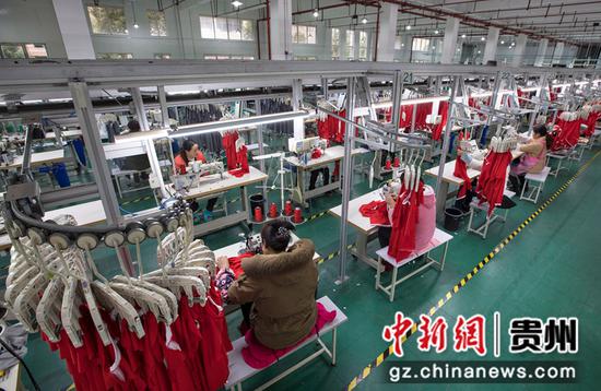 2021年12月14日，工人在贵州省黔西市经济开发区扶贫基地一家制衣企业的生产线上加工服饰。