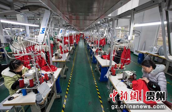 2021年12月14日，工人在贵州省黔西市经济开发区扶贫基地一家制衣企业的生产线上加工服饰。