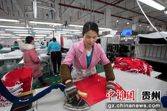 2021年12月14日，工人在贵州省黔西市经济开发区扶贫基地一家制衣企业的生产线上熨烫服饰。