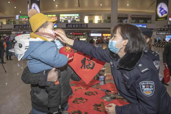在安全宣传活动现场民警小姐姐在送上“福”字后不忘为小旅客戴好口罩。