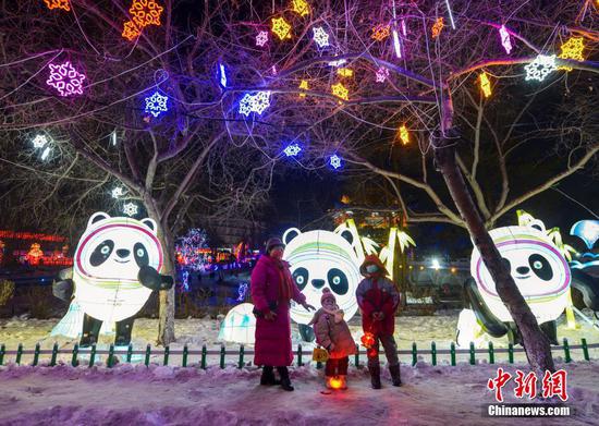 1月18日晚，新疆乌鲁木齐市人民公园，众多市民前来观赏大型花灯冰雕展。据介绍，该公园于日前推出迎春游园会，45组自贡花灯和25组亮化灯饰分布整个园区，同时设计雕刻了40多件冰雕作品，吸引众多市民前往观赏，游玩。图为市民在北京冬奥会吉祥物“冰墩墩”为造型的花灯前留影。中新社记者 刘新 摄

