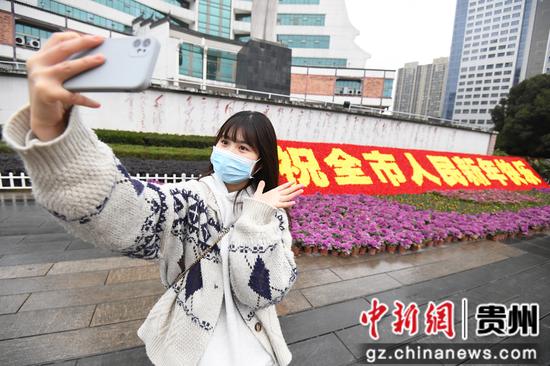 一位市民正在贵阳市筑城广场（南广场）迎春主题花坛前自拍留影。