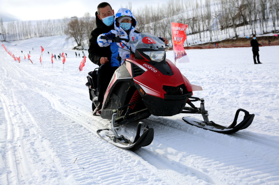 一位游客带着孩子在察布查尔县努拉洪滑雪场驾驶雪地摩托车游玩。华岩明摄