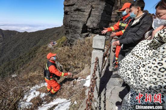 2月14日，一名消防救援人员在梵净山蘑菇石下帮助游客找掉落的物品。　瞿宏伦 摄