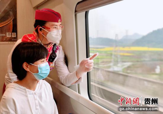动车乘务员正在为乘车旅客介绍乘坐高铁驶过的油菜花景点。 王登 摄