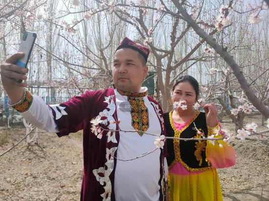 3月31日，阿克苏市民身穿少数民族服饰在杏花园内拍照。贾维霞 摄