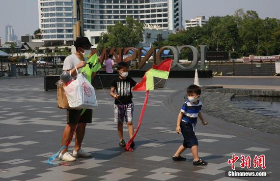 4月14日，泰国曼谷，一位市民带着孩子放风筝。时值泰历新年泼水节（宋干节）假期，曼谷街头不见“水花四溅”的景象。由于疫情原因，泰国政府规定今年泼水节不得进行泼水、相互抹粉等活动，但可以举行传统文化活动。中新社记者 王国安 摄