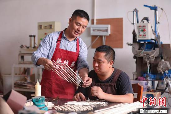 6月4日，张维义(左)在和工作室成员探讨吉他面板音梁制作细节。　瞿宏伦 摄