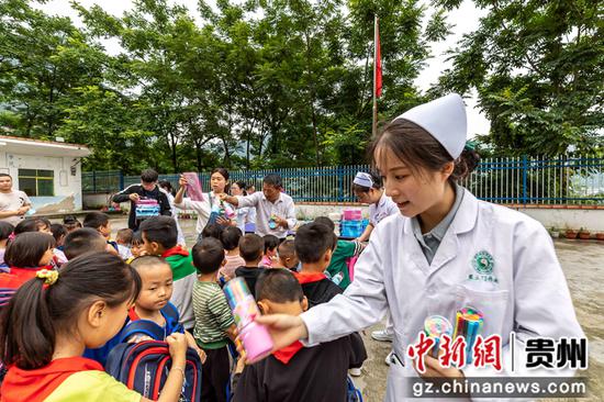 贵州省黔西市中医医院医务人员给学生发放书包文具。