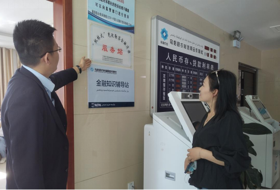 图为乌恰县农信社营业部工作人员给客户指引“枫桥式”金融消保服务站标识。 王慧 摄