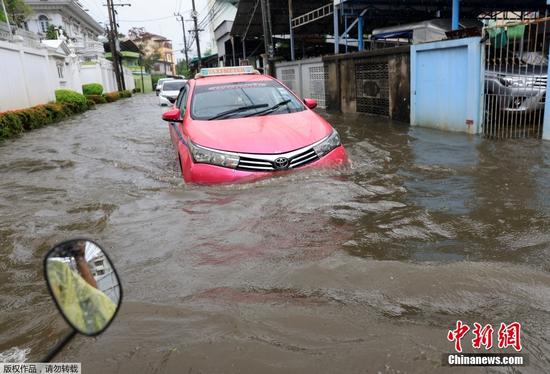当地时间7月21日，泰国曼谷因近日出现持续性强降雨，多个区域内的单日降水量创下数十年来最高纪录，导致城市内涝严重，居民涉水出行。图为大雨过后，车辆行驶在被洪水淹没的道路上。
