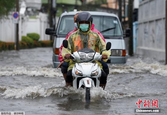 当地时间7月21日，泰国曼谷因近日出现持续性强降雨，多个区域内的单日降水量创下数十年来最高纪录，导致城市内涝严重，居民涉水出行。图为大雨过后，人们骑着摩托车在被洪水淹没的道路上蹚水前进。