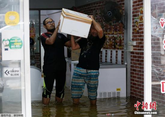 当地时间7月21日，泰国曼谷因近日出现持续性强降雨，多个区域内的单日降水量创下数十年来最高纪录，导致城市内涝严重，居民涉水出行。图为大雨过后，人们从被洪水淹没的杂货店里搬运东西。