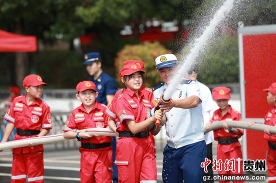 图为消防员带领学生体验水枪喷水。
