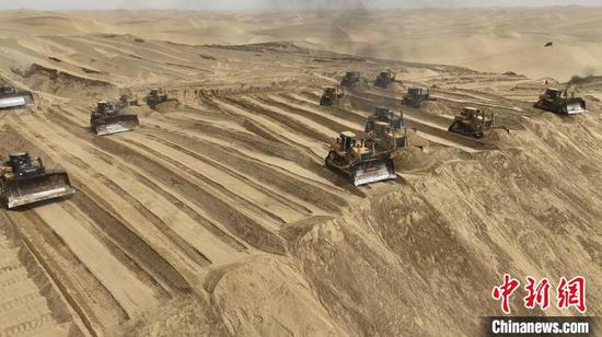 大型推土机并排在黄沙中平整高大沙丘，场面震撼。　赵志伟 摄