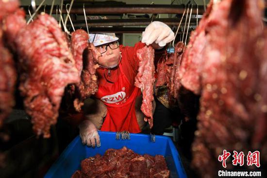 工人在贵州省江口县一家旅游食品加工作坊，把腌制好的牛肉进行烘烤。　李鹤 摄