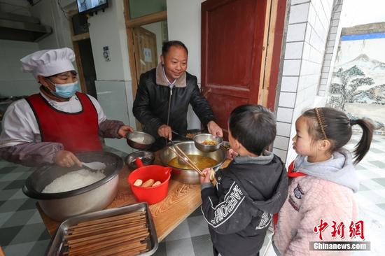 2月15日，杨朝俊在给学生盛营养午餐。