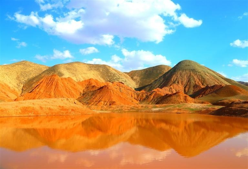 在新疆昌吉州阜康市南部山区水磨河河畔的小红沟，春日暖阳里的山地丘陵呈现出深浅不一、五彩斑斓的色带。
