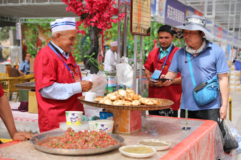 游客在岳普湖美食展位購(gòu)買(mǎi)岳普湖烤包子。 吳成昱攝