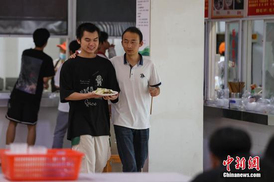 9月7日，贵州省惠水县，罗强（右）在食堂协助学生取餐。