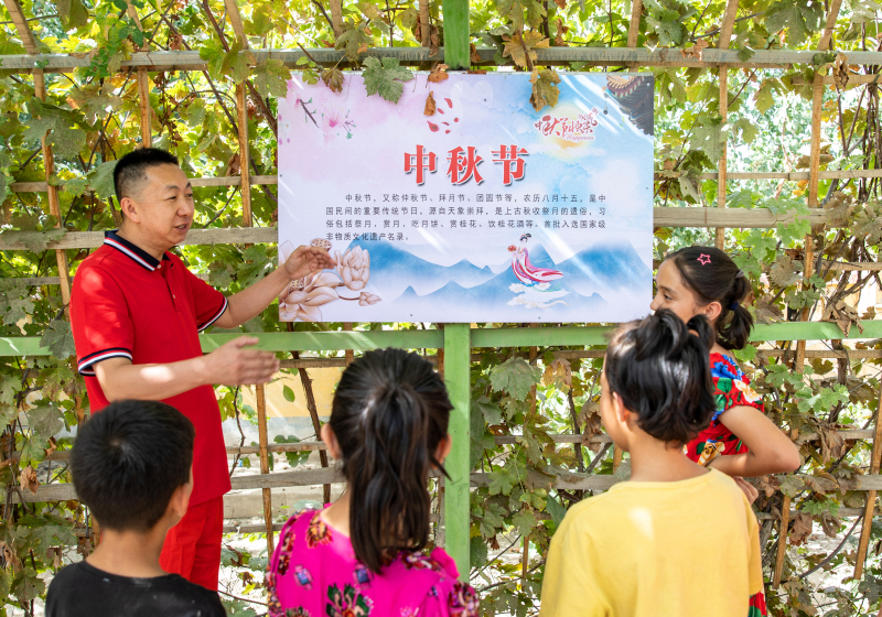在泽普县依克苏乡托万恰喀村文化长廊，新疆油田公司驻南疆“访惠聚”工作队队员（左一）给孩子们宣讲中华传统文化。