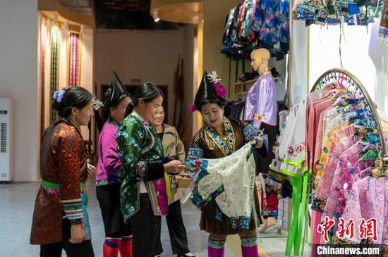 韦祖英(右一)在公司展示厅向客人介绍苗族服装。吴德军 摄