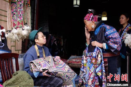 图为苗族绣娘潘玉珍为台湾游客林宜静介绍苗绣服饰。周燕玲摄