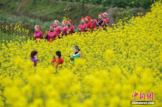 图为民众身着苗族服饰在油菜花田进行拍照。