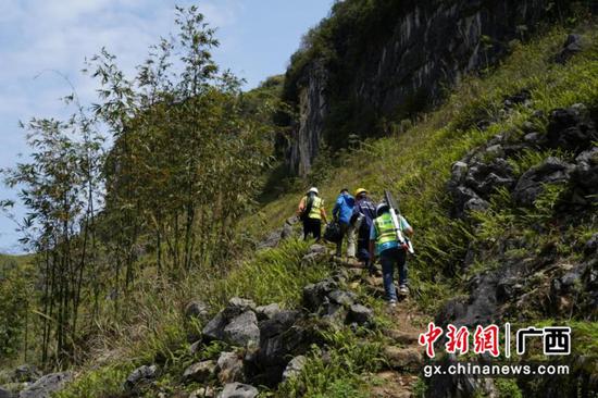 网络建设小组肩挑背扛工具和皮线光缆，沿着陡峭崎岖的山路向上攀爬。