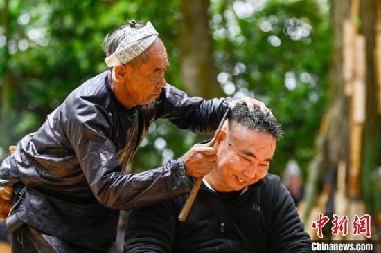 一名游客在贵州省从江县丙妹镇岜沙苗寨景区体验镰刀剃头。吴德军 摄