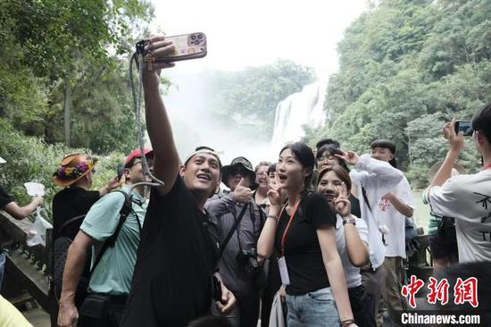 图为游客在贵州黄果树瀑布前合影。陈洋昕 摄