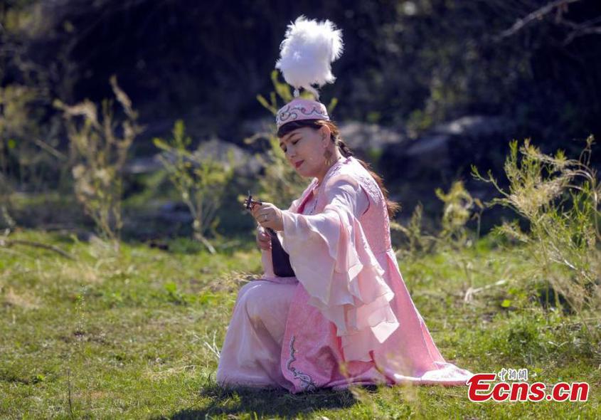 An artist adjusts her tamboura at a park in Urumqi, northwest China's Xinjiang Uyghur Autonomous Region, Aug. 3, 2024. (Photo: China News Service/Liu Xin)