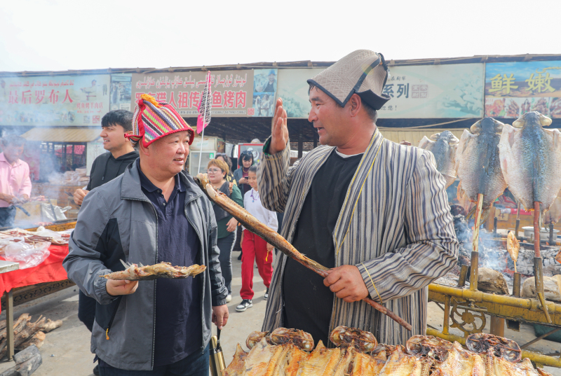 10月4日，游客在新疆尉犁縣羅布人村寨景區(qū)美食區(qū)烤魚(yú)。汪志鵬 攝