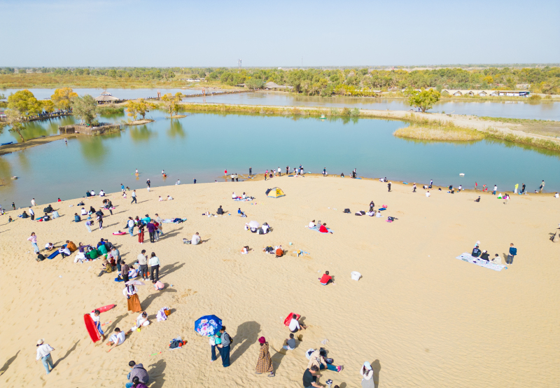 10月4日，在新疆尉犁縣羅布人村寨景區(qū)，游客在沙海胡楊河流之間暢游，享受假日時(shí)光。 汪志鵬 攝