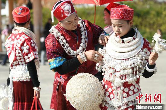 图为黄平“芦笙会”现场，一名苗族女孩在家人的帮助下穿戴苗族银饰。陈孝新摄