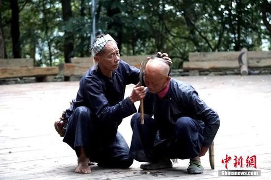 从江县丙妹镇岜沙苗寨，村民在向游客展示传统的“镰刀剃头”技艺。张素 摄