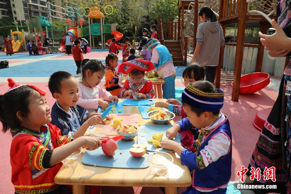 3月27日，在广西南宁市邕宁区一所幼儿园内，师生身着民族服装参加“三月三”民俗活动，通过体验民俗美食一条街、民俗手工一条街的形式，欢度充满童趣与文化气息的“三月三”。图为小朋友在切水果制作酸嘢。卢虹灵 摄