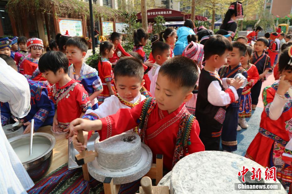 3月27日，在广西南宁市邕宁区一所幼儿园内，师生身着民族服装参加“三月三”民俗活动，通过体验民俗美食一条街、民俗手工一条街的形式，欢度充满童趣与文化气息的“三月三”。图为小朋友在磨米浆制作卷筒粉。卢虹灵 摄